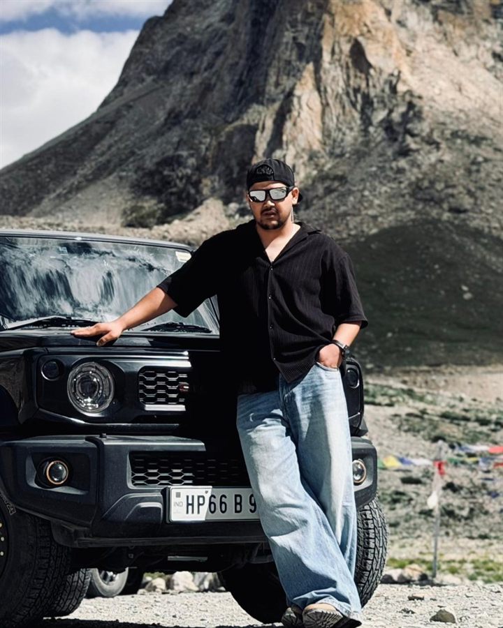 Dinesh Thakur, tail rider at Indian Moto Adventures, beside a black Suzuki Jimny in the mountains