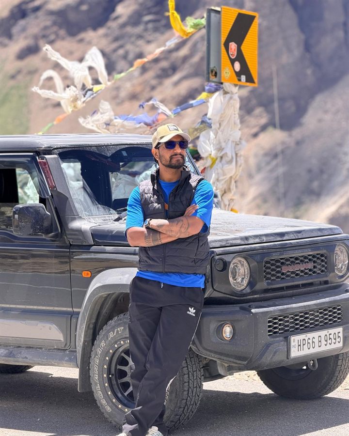 Ritesh Thakur, head of the riding team at Indian Moto Adventures, beside a black Suzuki Jimny on a mountain road