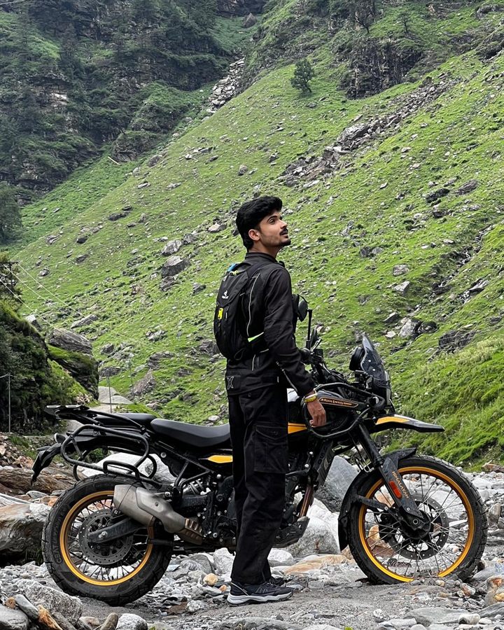 Vinayak Thakur of the Indian Moto Adventures media team with a Royal Enfield Himalayan in a green mountain valley